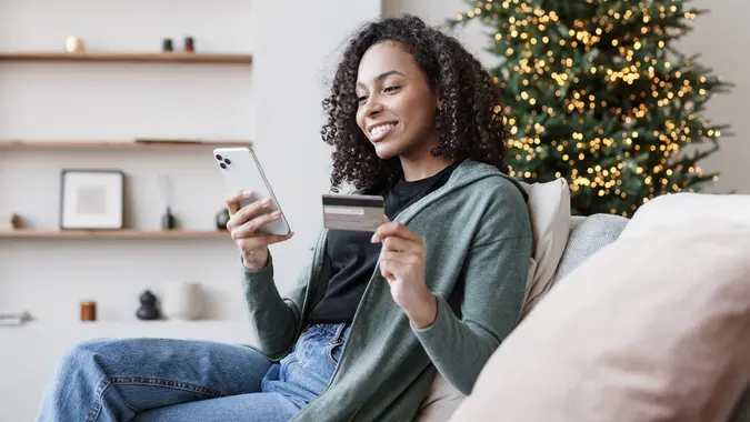 young-woman-ordering-holiday-gifts-christmas-tree-smartphone-credit-card_iStock-1439734850